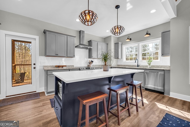 kitchen featuring light wood finished floors, a breakfast bar, decorative backsplash, appliances with stainless steel finishes, and wall chimney range hood