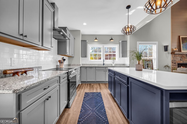 kitchen featuring light wood-style floors, wall chimney exhaust hood, stainless steel electric range, and plenty of natural light