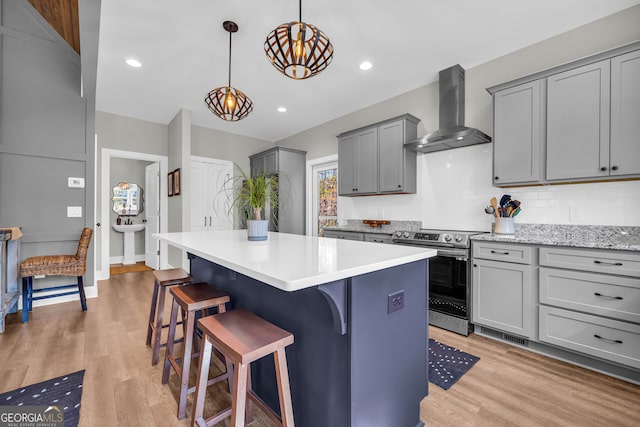 kitchen featuring wall chimney range hood, stainless steel electric range, gray cabinets, and light wood finished floors