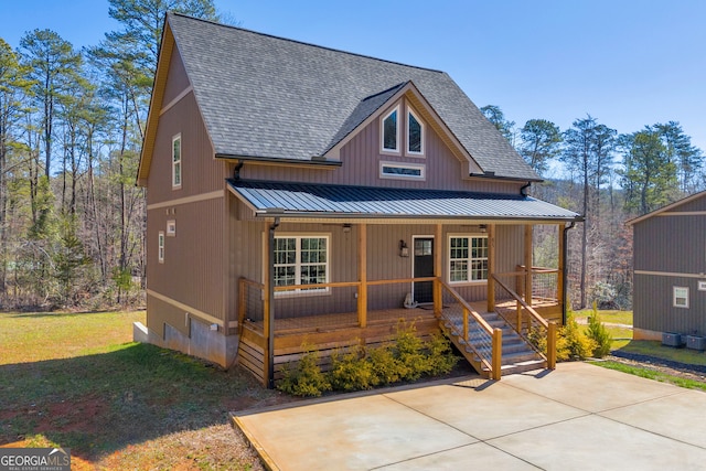 rustic home featuring a standing seam roof, covered porch, a front yard, a shingled roof, and metal roof