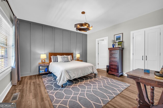 bedroom with a decorative wall, visible vents, and wood finished floors