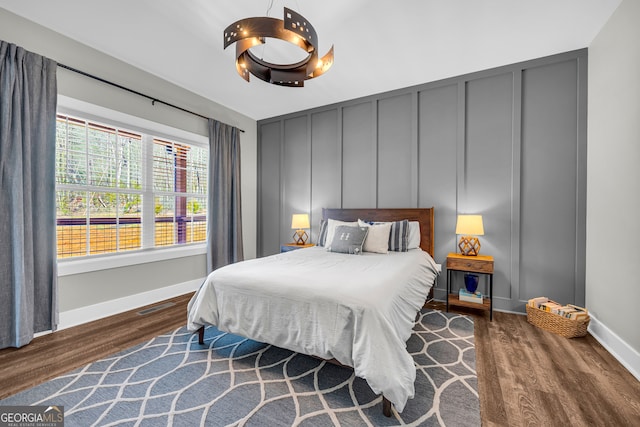 bedroom featuring a decorative wall, baseboards, visible vents, and wood finished floors