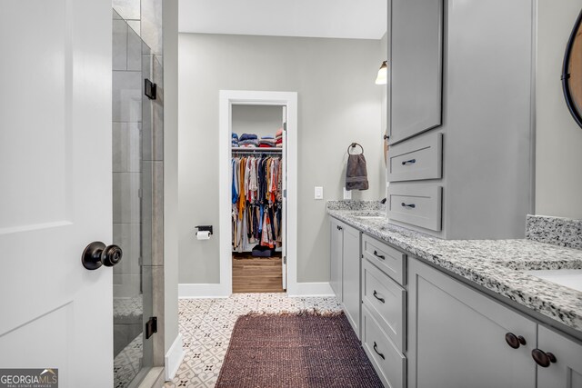 full bath featuring double vanity, baseboards, a stall shower, and a spacious closet