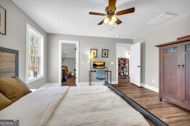 bedroom with visible vents, a walk in closet, wood finished floors, baseboards, and ceiling fan