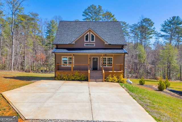 chalet / cabin featuring a porch, metal roof, a front lawn, and roof with shingles