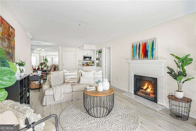 living area featuring light wood finished floors, a warm lit fireplace, crown molding, and baseboards