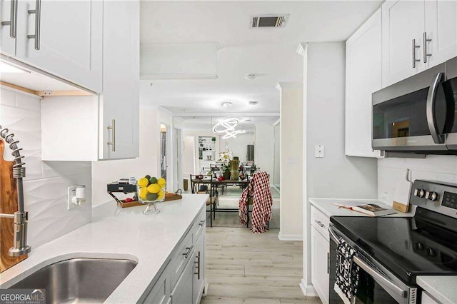 kitchen with tasteful backsplash, visible vents, light wood finished floors, white cabinets, and stainless steel appliances