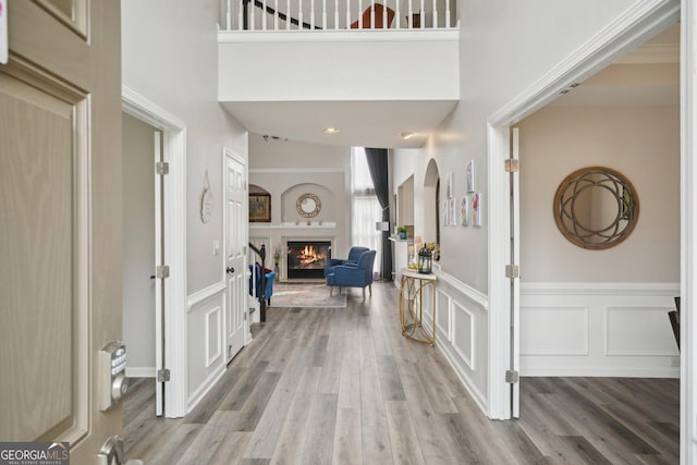 entrance foyer featuring a lit fireplace, wainscoting, wood finished floors, arched walkways, and a decorative wall