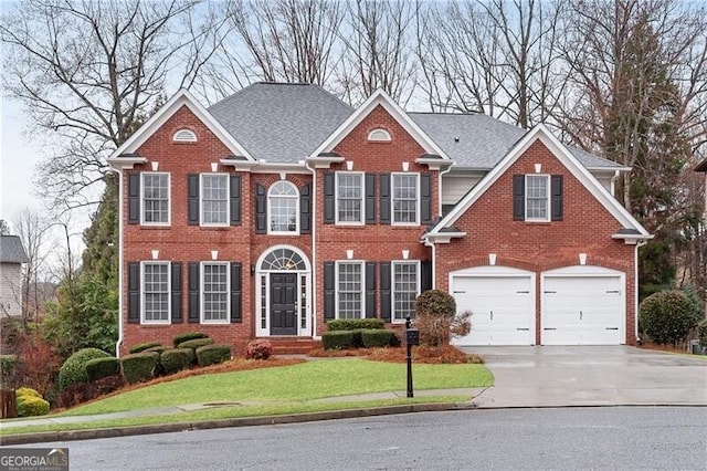 colonial home with a garage, a front yard, brick siding, and driveway