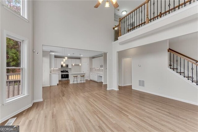 unfurnished living room with light wood-type flooring, visible vents, stairway, baseboards, and ceiling fan