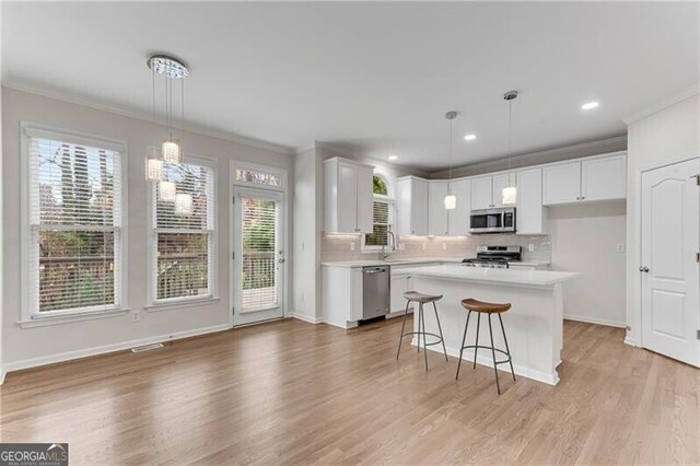kitchen featuring backsplash, light countertops, ornamental molding, stainless steel appliances, and white cabinetry