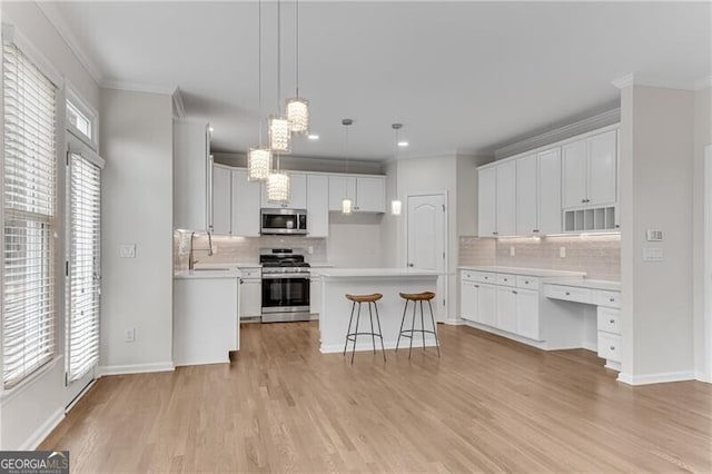 kitchen with light wood-type flooring, appliances with stainless steel finishes, ornamental molding, and white cabinets