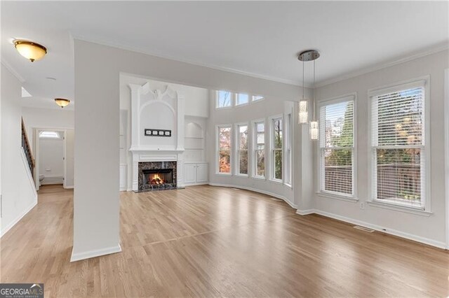 unfurnished living room with built in shelves, baseboards, light wood-type flooring, a premium fireplace, and ornamental molding