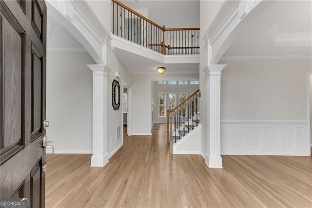 entrance foyer featuring light wood-type flooring, decorative columns, arched walkways, and ornamental molding