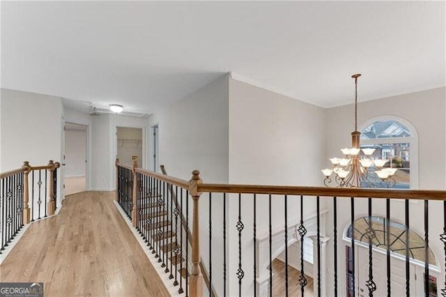 hallway featuring light wood finished floors, a notable chandelier, an upstairs landing, and ornamental molding