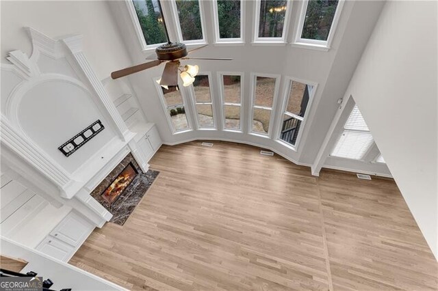 unfurnished living room with visible vents, a fireplace with flush hearth, light wood-style floors, and a towering ceiling