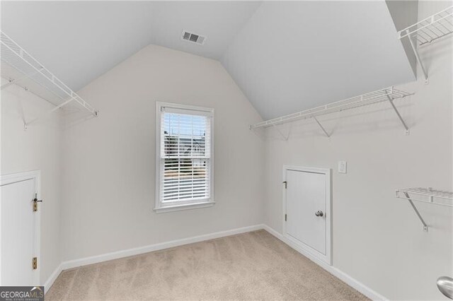 spacious closet with visible vents, lofted ceiling, and light colored carpet