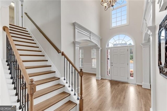foyer with wood finished floors, baseboards, ornate columns, a high ceiling, and a notable chandelier