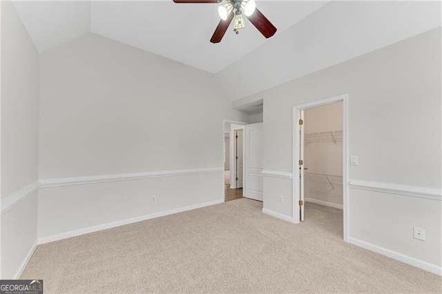 unfurnished bedroom with carpet flooring, baseboards, a walk in closet, and lofted ceiling