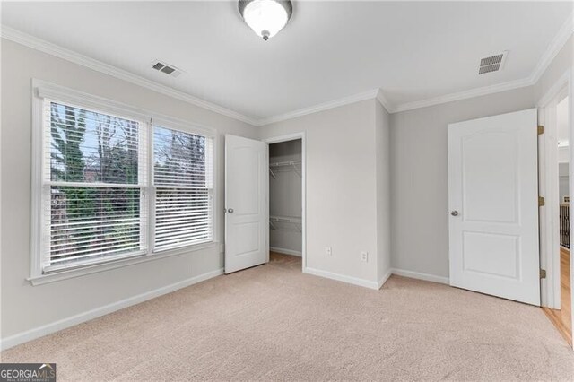 unfurnished bedroom with visible vents, light colored carpet, crown molding, and baseboards