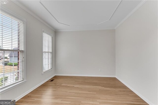 empty room featuring crown molding, light wood-style flooring, visible vents, and baseboards