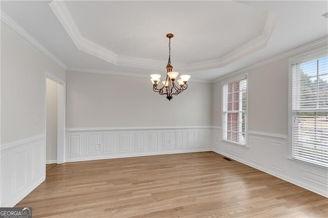 unfurnished room featuring visible vents, light wood finished floors, a tray ceiling, wainscoting, and a notable chandelier