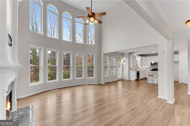 unfurnished living room featuring a fireplace, baseboards, light wood-type flooring, and a ceiling fan