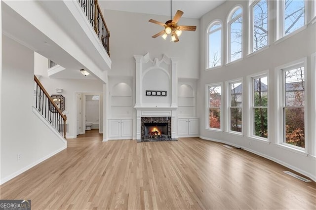 unfurnished living room with visible vents, light wood-style flooring, baseboards, and a premium fireplace