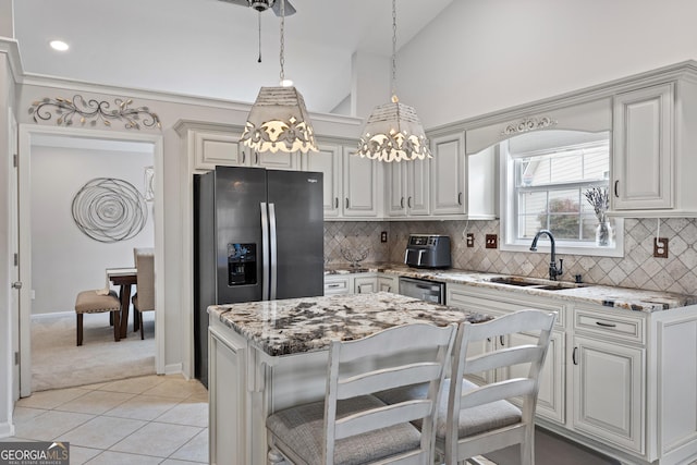 kitchen featuring a sink, light stone counters, stainless steel fridge, light tile patterned floors, and vaulted ceiling