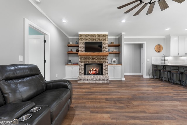 living room with a brick fireplace, baseboards, dark wood finished floors, ornamental molding, and a ceiling fan