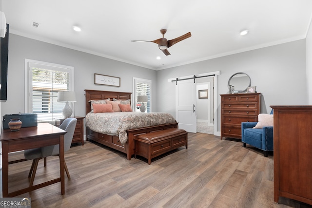 bedroom with a barn door, light wood-style flooring, multiple windows, and visible vents