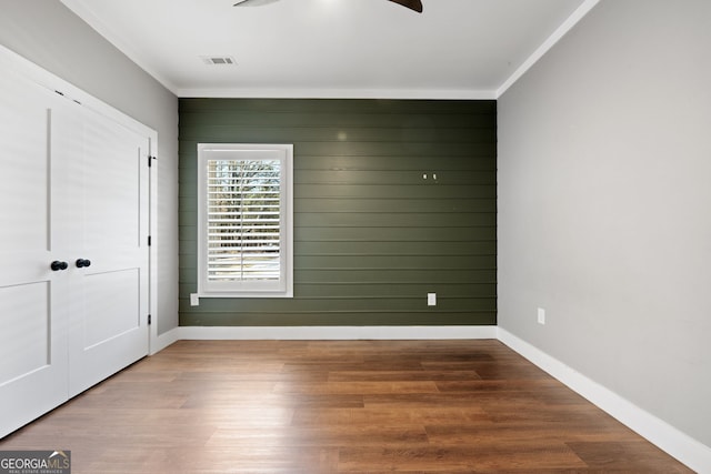 spare room with visible vents, baseboards, wood finished floors, and ornamental molding