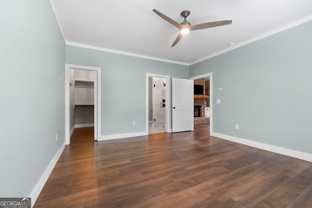 unfurnished bedroom featuring wood finished floors, baseboards, a fireplace, ornamental molding, and a walk in closet