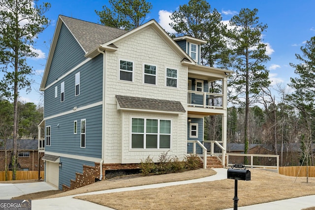 view of front facade with fence, roof with shingles, a garage, a balcony, and driveway