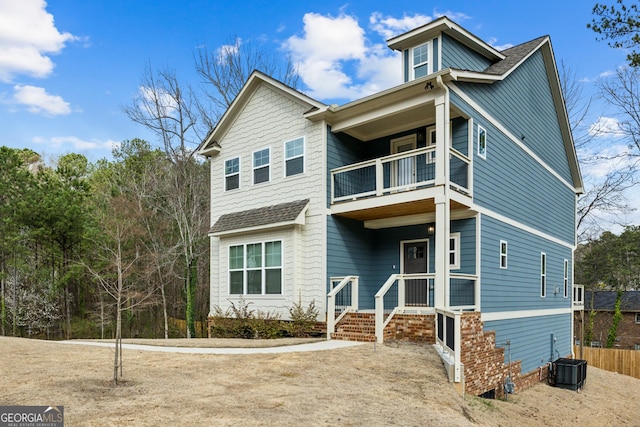 view of front of house with a balcony, central AC unit, fence, and roof with shingles