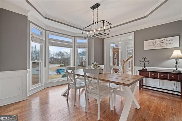 dining space with crown molding, wood finished floors, a tray ceiling, and wainscoting