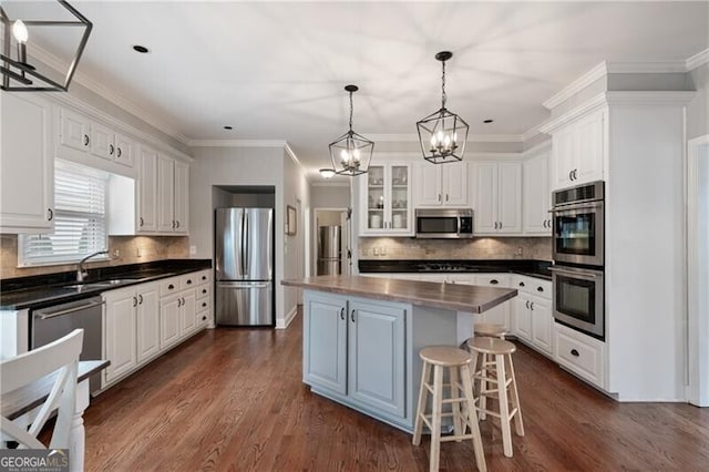 kitchen featuring a kitchen island, a sink, white cabinets, appliances with stainless steel finishes, and dark countertops