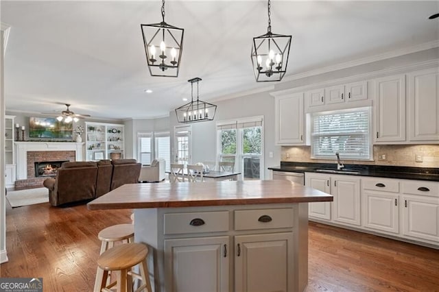 kitchen with crown molding, a brick fireplace, light wood-style floors, and a sink