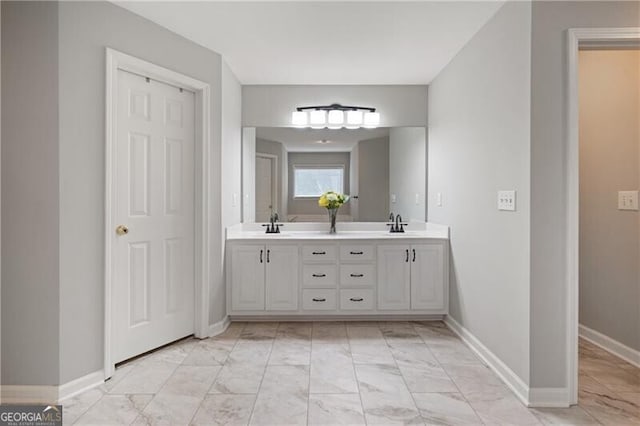 bathroom featuring a sink, baseboards, marble finish floor, and double vanity