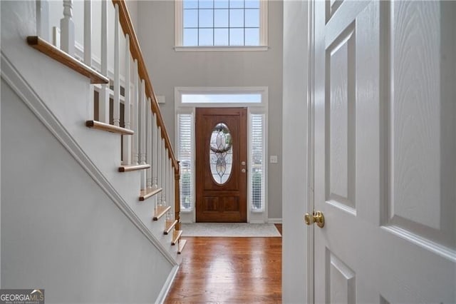 foyer entrance with plenty of natural light, stairs, a towering ceiling, and wood finished floors