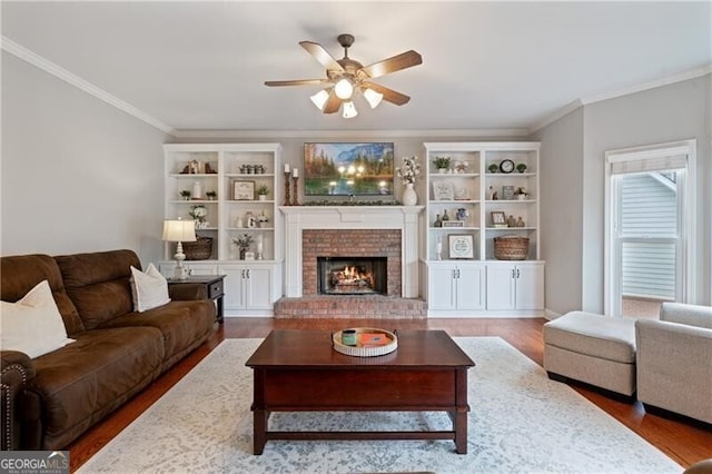 living room with a fireplace, a ceiling fan, wood finished floors, and ornamental molding