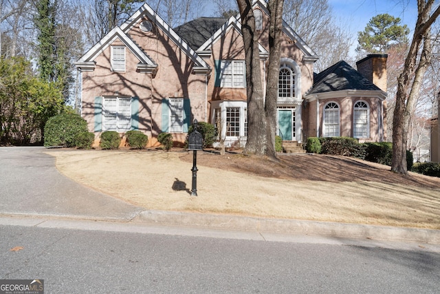 view of front of house featuring brick siding, a chimney, and a shingled roof