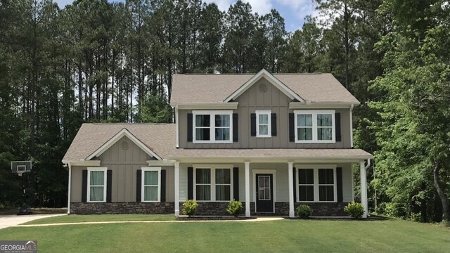 view of front facade with board and batten siding, a front lawn, stone siding, and roof with shingles