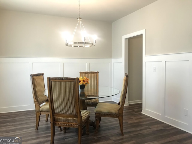 dining room featuring dark wood finished floors, a decorative wall, a wainscoted wall, and a chandelier