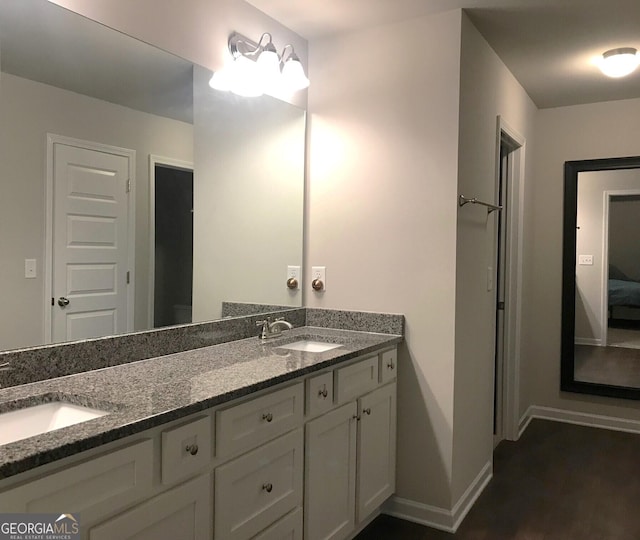 ensuite bathroom with double vanity, connected bathroom, baseboards, and a sink