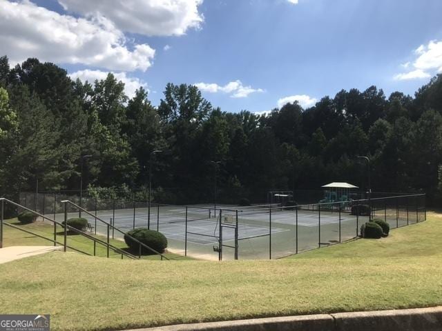 view of sport court with a lawn, fence, and a view of trees