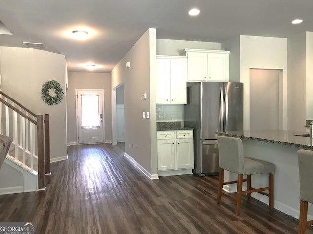 kitchen with dark stone countertops, visible vents, dark wood-style flooring, freestanding refrigerator, and backsplash