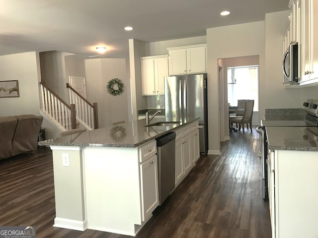 kitchen featuring dark stone counters, dark wood-style flooring, a sink, appliances with stainless steel finishes, and open floor plan