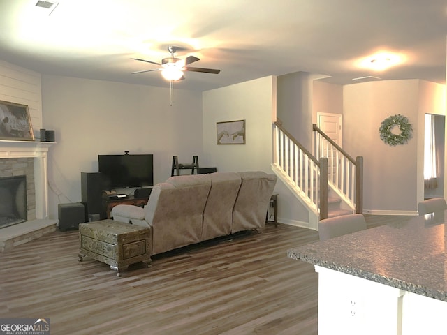 living room with visible vents, a fireplace with raised hearth, ceiling fan, stairs, and wood finished floors