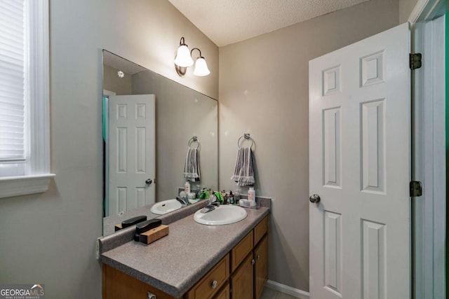 bathroom with a textured ceiling, vanity, and baseboards